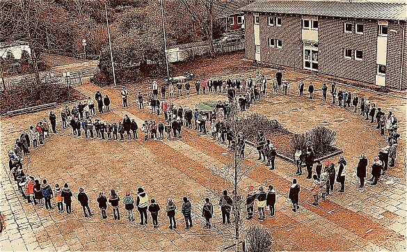 Das Foto zeigt Personen auf dem Schulhof, die sich als Friedenszeichen aufgestellt haben