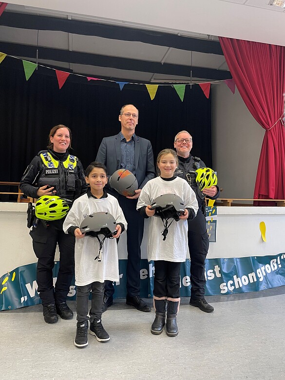 Gruppenfoto mit Bildungssenator, einer Polizistin, einem Polizisten und zwei Schulkindern. Alle haben einen Fahrradhelm in der Hand.